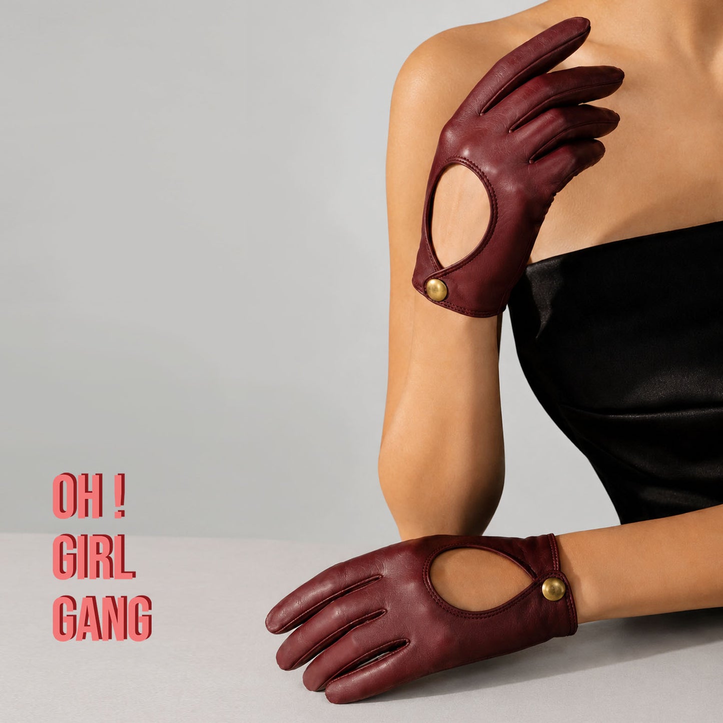Pair of genuine leather driving gloves in burgundy, white, black, featuring an elegant open-back teardrop cutout with snap-button closure. Soft premium leather with a classic vintage-inspired design, displayed on a light grey background.